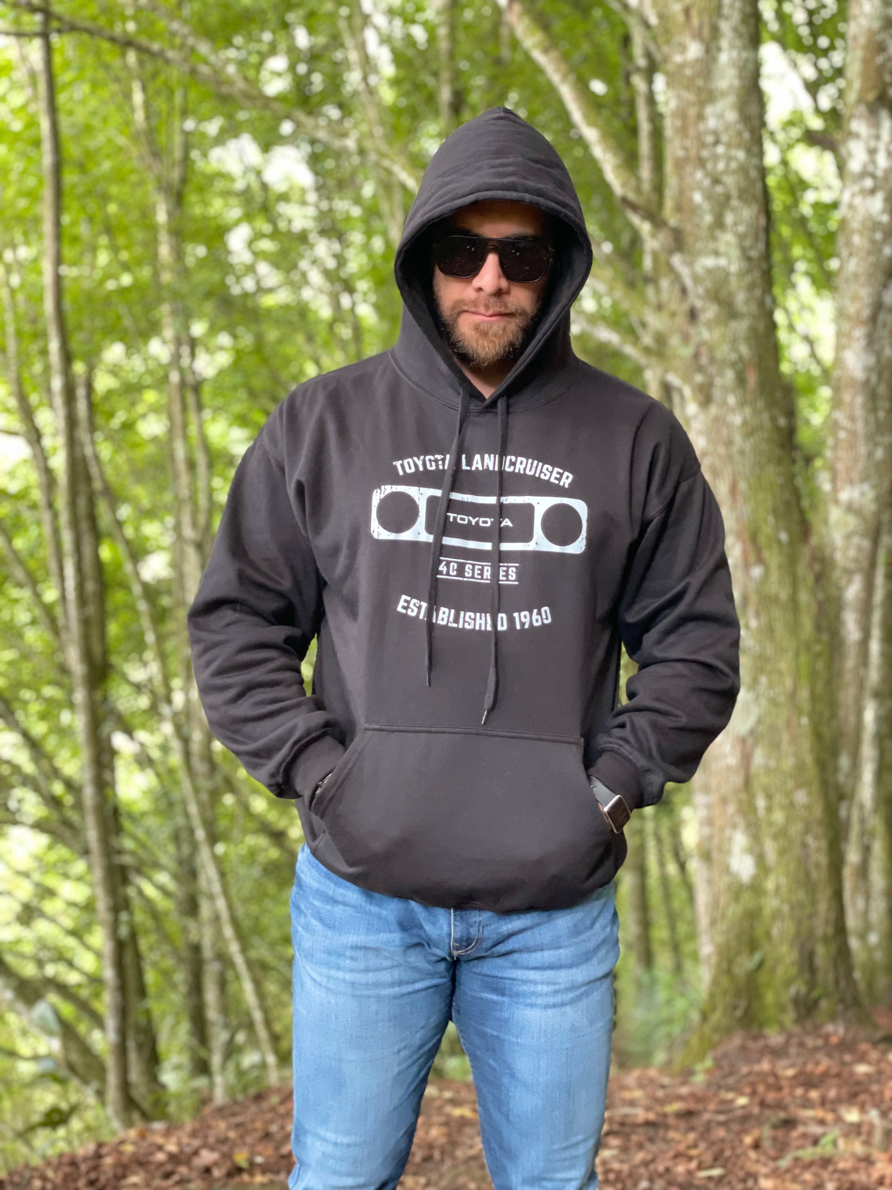 Nuestro modelo usando un hoddie de color negro con un estampado blanco en un fodo boscoso